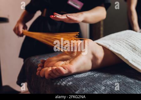 Massage der weiblichen Füße mit Bambusstäbchen Stockfoto