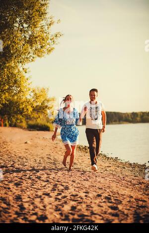 Glückliches junges Paar, das in Kleid am Strand läuft Stockfoto