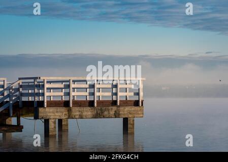 Steg auf einem See mit Nebel. Holzstruktur auf dem Wasser. Sonnenaufgang und Nebel über dem Wasser. Stockfoto