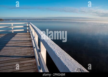 Steg auf einem See mit Nebel. Holzstruktur auf dem Wasser. Sonnenaufgang und Nebel über dem Wasser. Stockfoto