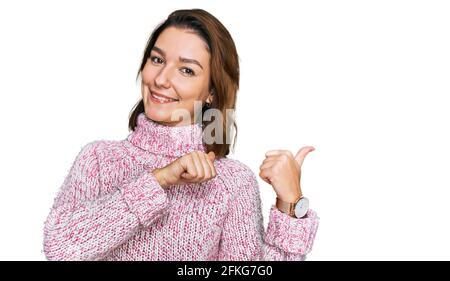 Junge kaukasische Mädchen trägt Wolle Winter Pullover zeigt auf den Rücken hinter mit Hand und Daumen nach oben, lächelnd zuversichtlich Stockfoto