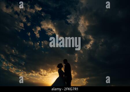Silhouetten der Braut und des Bräutigams, die sich am Sonnenuntergang umarmen Am Abend Stockfoto