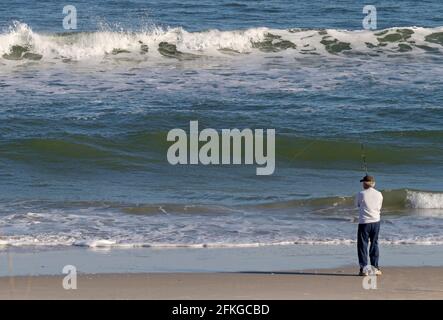 Älterer weißer Mann steht am Strand und fischt hinein Das turbulente Meer an einem sonnigen Tag Stockfoto