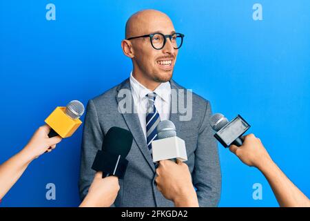 Kahlköpfiger Mann mit Bart, der von Reportern interviewt wird, die Mikrofone zur Seite halten, die Profilpose mit natürlichem Gesicht entspannen und selbstbewusstes Lächeln zeigen. Stockfoto