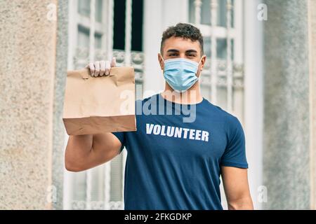 Junger hispanischer Freiwilliger in der Stadt mit einer medizinischen Maske, die einen Liefersack hält. Stockfoto