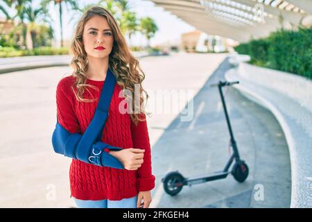 Junge blonde Mädchen mit ernsten Ausdruck verletzt mit Arm Sling stehen im Park. Stockfoto