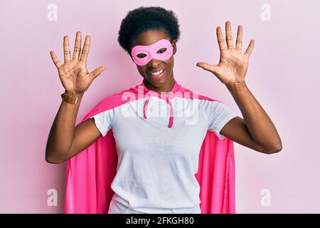 Junge afroamerikanische Mädchen trägt Superhelden-Maske und Cape Kostüm zeigt und zeigt mit den Fingern Nummer zehn, während lächelnd zuversichtlich und glücklich. Stockfoto