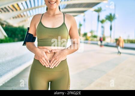 Junge blonde Sportlerin trägt Sportkleidung mit Händen auf dem Bauch in der Stadt. Stockfoto