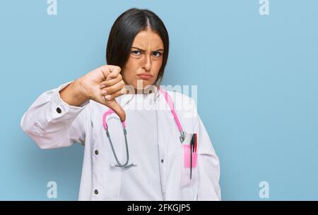 Schöne hispanische Frau trägt Arzt Uniform und Stethoskop, die unglücklich und wütend aussagt und Ablehnung zeigt und negativ mit Daumen nach unten Geste. Schlecht Stockfoto