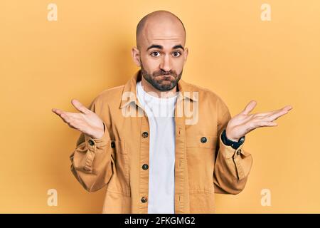 Junger kahlköpfiger Mann in lässiger Kleidung, ahnungsloser und verwirrter Ausdruck mit erhobenen Armen und Händen. Zweifel-Konzept. Stockfoto