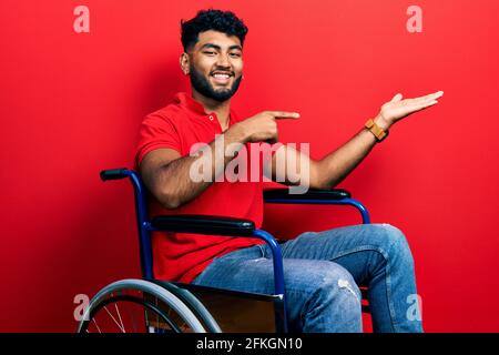 Arabischer Mann mit Bart sitzt auf dem Rollstuhl erstaunt und lächelt zur Kamera, während er mit der Hand zeigt und mit dem Finger zeigt. Stockfoto