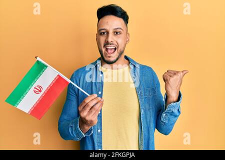Junger araber mit der iranischen Flagge, auf die der Daumen zeigt Die Seite lächelt glücklich mit offenem Mund Stockfoto