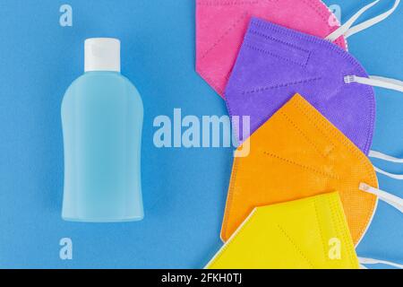 Handalkoholdesinfektionsmittel und verschiedene Farben FFP2 oder N95 Gesichtsmasken Atemschutzmasken. Auf blauem Hintergrund. Flache Schicht aus der Draufsicht. Schutz vor Covid-Virus d Stockfoto