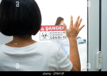 Eine Frau, die vor dem Quarantäneraum steht und eine Hand auf den Spiegel legt, während sie auf die Untersuchungsergebnisse wartet, hat eine Menge Angst. Konz Stockfoto