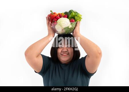 Glückliche übergewichtige asiatische Frau, die einen Gemüskorb hält und auf einem isolierten weißen Hintergrund lächelt, kommt das Konzept der guten Gesundheit vom Essen einer Nutritiou Stockfoto