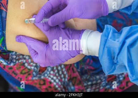 Nahaufnahme von behandelten Händen des Arztes, die einen Impfstoff in den Arm eines Patienten injizieren. Impfungs- und Coronavirus-Pandemiekonzept Stockfoto