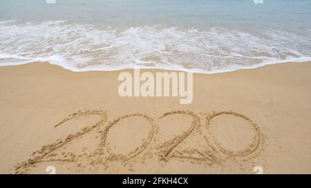 2020 Text am Strand, 2020-Jahres-Nachricht Hand geschrieben in Sand auf wunderschönen Strand Wellen krachen auf sandigen Ufer Hintergrund. Konzept für das neue Jahr. Stockfoto