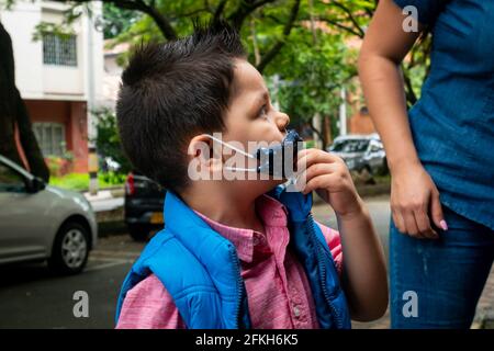 Medellin, Kolumbien - März 28 2021: Kleiner lateinischer Junge mit blauer Gesichtsmaske draußen Stockfoto