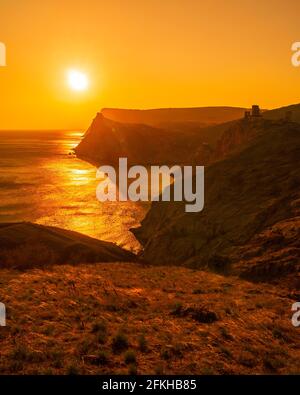 Ein rot brennender Sonnenuntergang mit dem Silhouett einer Klippe Und Burg über dem Meer Stockfoto