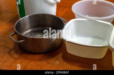 Verschiedene Container auf dem Holzboden des Hauses angeordnet. Zur Aufnahme von Regenwasser, das bei starkem Regen vom Dach austritt. Stockfoto