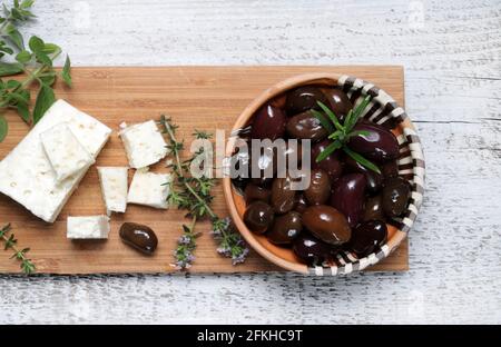 Schwarze Oliven, Feta-Käse und aromatische Kräuter auf Holzschneidebrett. Direkt darüber. Stockfoto