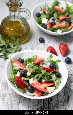 Gesunder Salat mit Erdbeeren, Blaubeeren, Rucola und Feta-Käse auf weißem Teller. Stockfoto