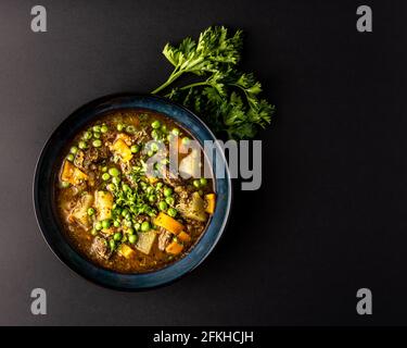 Rindfleisch-Eintopf mit Kartoffeln und Gemüse auf einem Teller Ein dunkler Tisch Stockfoto