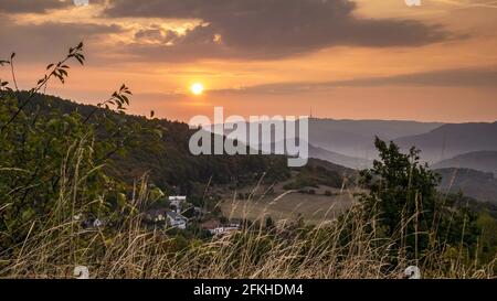 Goldener Sonnenaufgang über einer hügeligen Landschaft mit Nebel im Tal, bewölktem Himmel und einem Funkturm am Horizont Stockfoto