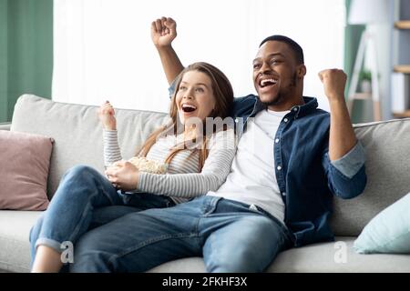 Home Entertainment. Glücklich Interracial Paar Fernsehen Und Jubeln Sport Zu Hause Stockfoto