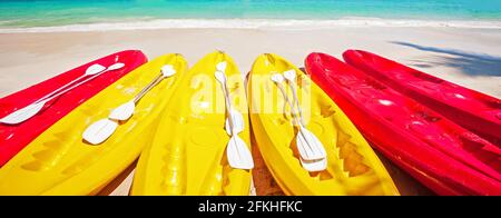 Farbenfrohe Kajaks mit Paddeln an einem tropischen Strand im sonnigen Sommer, helle Meereswellen und türkisfarbenes Meerwasser im Hintergrund. Urlaubskonzept Stockfoto