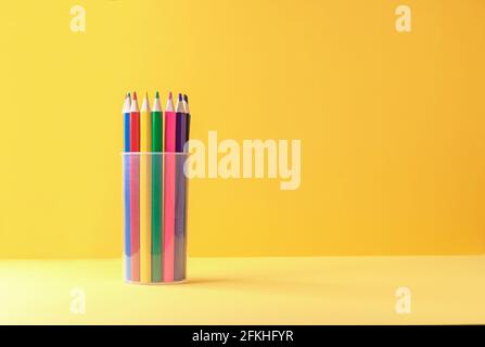 Buntstifte in einem Plastikbecher auf gelb-orangem Hintergrund. Stockfoto