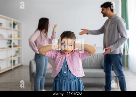 Konzept der Kindheitstraumata. Verärgerte arabische Mädchen, die Ohren mit Händen bedeckt, um den Konflikten der Eltern nicht zuzuhören Stockfoto