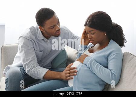 Schwarze schwangere Dame, die sich krank fühlt, besorgter Ehemann, der neben ihr sitzt Stockfoto