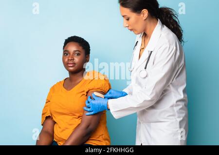 Arzt, Der Gipsstreifen Nach Der Injektion Auf Den Arm Aufsetzt, Blauer Hintergrund Stockfoto