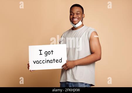 Happy African man Holding Poster Ich wurde geimpft, Beige Hintergrund Stockfoto