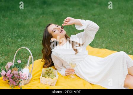 Eine schöne junge Frau liegt auf einer gelben Decke auf dem Gras und hält ein Glas Wein Stockfoto
