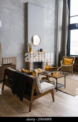 Interieur im skandinavischen Stil mit Kamin, Rattanstuhl in den trendigen Farben 2021 grau und gelb Stockfoto