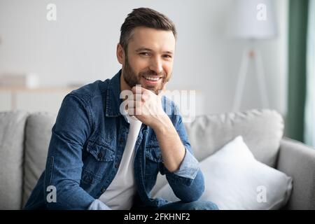 Nahaufnahme eines bärtigen Mannes, der auf der Couch sitzt und lächelt Stockfoto