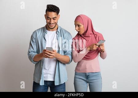 Eifersüchtige muslimische Frau im Hijab, die das Mobiltelefon ihres Freundes anschaut und Misstrauen leidet Stockfoto