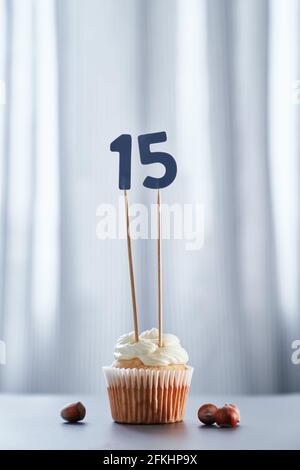 Hausgemachter leckerer Cupcake oder Muffin mit Nummer 15 fünfzehn und Haselnüssen auf dem Tisch und hellem Hintergrund. Geburtstag oder Jubiläum Grußkarte Konzept. Hochwertige vertikale Fotos Stockfoto