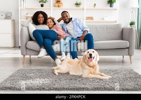 Glückliche schwarze Familie, die im Wohnzimmer mit Hund sitzt Stockfoto