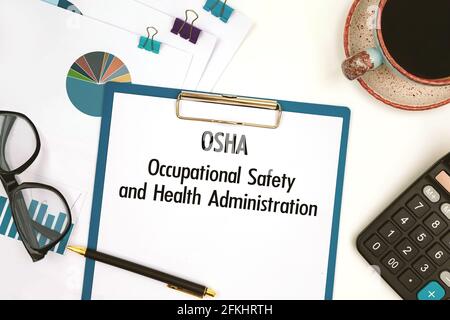 Papier mit Text OSHA - Occupational Safety and Health Administration auf dem Bürotisch, Rechner und Tasse Kaffee Stockfoto