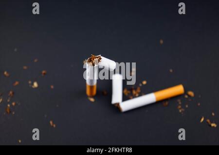 Zerbrechende, zerstörende Zigaretten, rauchender Tabak lag flach auf schwarzem Grunge-Textur-Hintergrund. Für alle Rauchkonzepte oder den Welt-No-Tobacco-Tag. Stockfoto