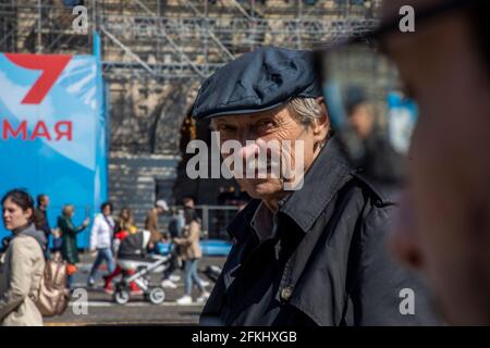 Moskau, Russland. 1. Mai, 2021 Menschen gehen auf dem Roten Platz in Moskau während des Feiertages des Labor Day, auch bekannt als 1. Mai, auf dem Hintergrund eines Plakats für den Tag des Sieges (9. Mai) geschmückt. Im Jahr 2021 beschlossen die Stadtbehörden in Moskau, die traditionelle Demonstration am 1. Mai aufgrund der schwierigen epidemiologischen Situation mit dem neuartigen Coronavirus COVID-19 in der Region abzusagen Stockfoto