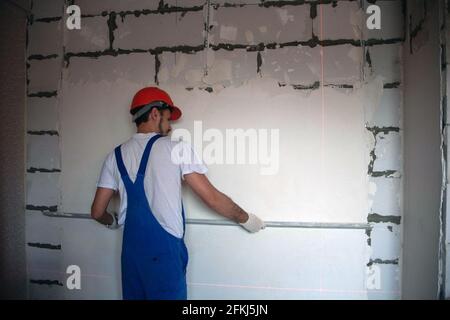 Arbeiten Sie an der Fertigstellung der Wände mit Mischungen aus Gips und Kitt beim Bau eines Hauses. bauarbeiter Verputzen Fassade des Hochhauses mit Kitt Messer. Nivellierung Steinwände Stockfoto