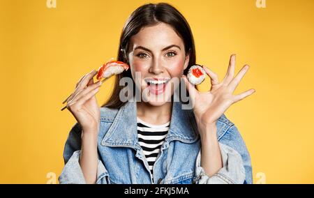 Glückliche Frau zeigt Sashimi und Makizushi. Mädchen essen Sushi-Rollen mit Essstäbchen und lächeln von erstaunlichen Rabatte zum Mitnehmen in japenese Stockfoto