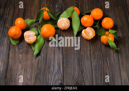 Ein paar frische Mandarinorangen, ganz, halbiert und geschält, mit Blättern, auf einem dunkelbraunen Tisch mit Holzstruktur. Gesunde vegane vegetarische Zitrusfrüchte, Vit Stockfoto