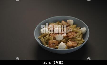 Pesto Penne mit gebratenen Garnelen und Mozzarella in blauer Schale auf schwarzem Hintergrund, breites Foto Stockfoto