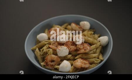 Pesto Penne mit gebratenen Garnelen und Mozzarella in blauer Schale auf schwarzem Hintergrund, breites Foto Stockfoto