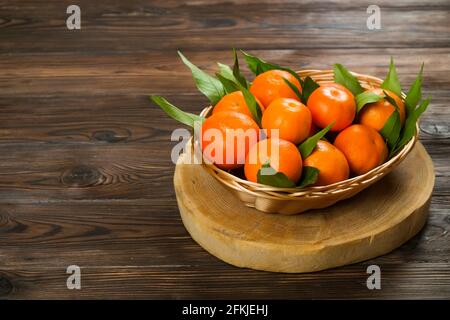 Korb mit frischen Mandarinenorangen, ganz, halbiert und geschält, mit Blättern, auf einem dunkelbraunen Tisch mit Holzstruktur. Gesunde vegane vegetarische Zitrusfrüchte, vi Stockfoto